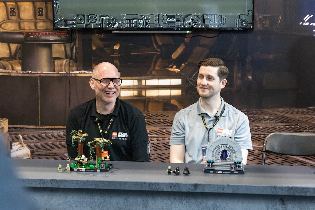 Two men sat at a table with lego sets in front of them